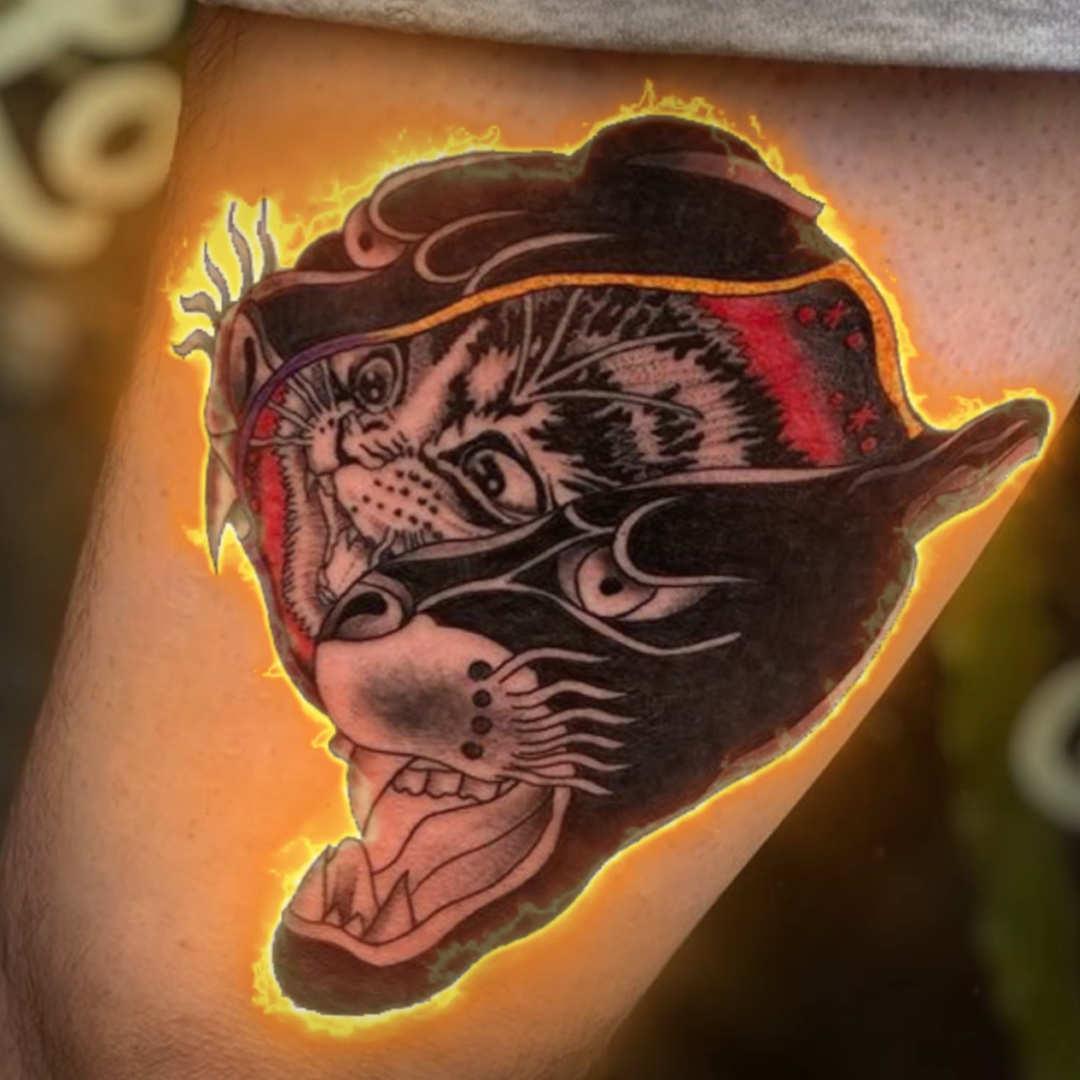 Een foto van een tattoo. De tattoo is een kitten verschuilt in het hoofd van een panter. De tattoo staat in de brand.